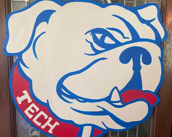 May include: A wooden bulldog-shaped sign with a white base, blue and red accents, and the word "TECH" in white. The sign is hanging by a white rope. The bulldog has a stern expression.