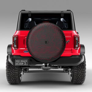 May include: Red Ford Bronco with a black spare tire cover featuring a red topographic design. The spare tire cover has the text "MUD DIGGER DESIGN CO." printed on it.