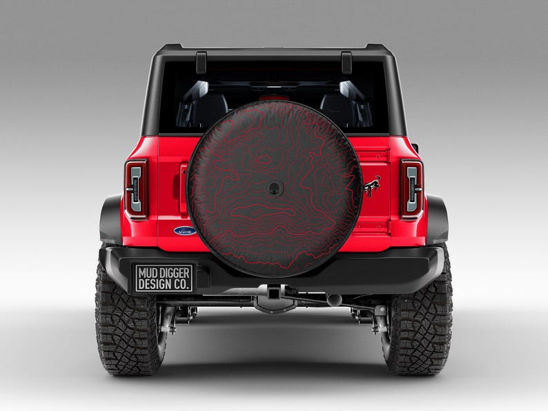 May include: Red Ford Bronco with a black spare tire cover featuring a red topographic design. The spare tire cover has the text "MUD DIGGER DESIGN CO." printed on it.
