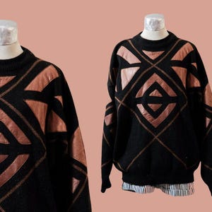 May include: A black sweater with a geometric pattern of brown leather. The sweater has a crew neck and long sleeves.