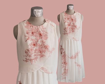 May include: A white sleeveless dress with a floral print in shades of pink. The dress has a layered skirt and a fitted bodice.