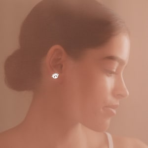 May include: A woman with brown hair wearing a white eye-shaped earring.