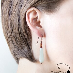 May include: A pair of dangle earrings with a light green teardrop-shaped bead and copper-colored beads and wire.