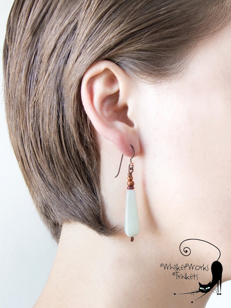 May include: A pair of dangle earrings with a light green teardrop-shaped bead and copper-colored beads and wire.