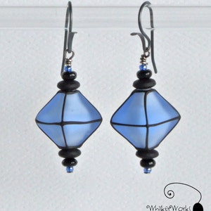 May include: A pair of blue and black glass earrings with a geometric diamond shape. The earrings are suspended from silver hooks.