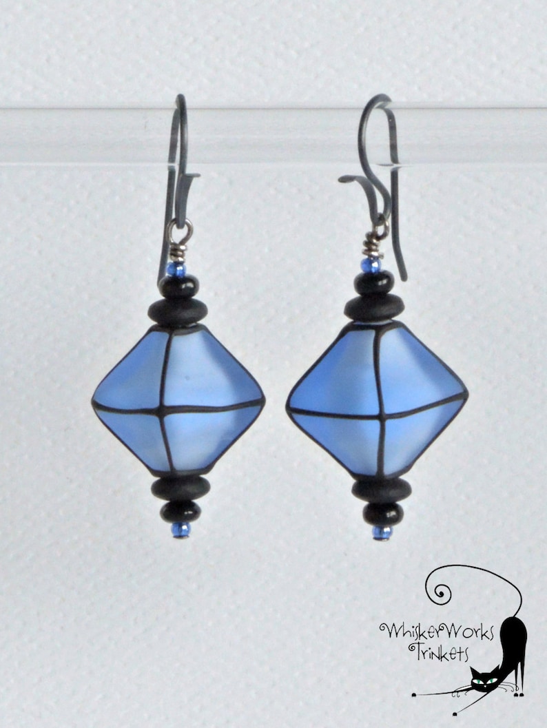 May include: A pair of blue and black glass earrings with a geometric diamond shape. The earrings are suspended from silver hooks.
