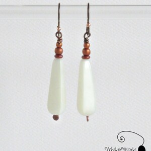 May include: A pair of white teardrop-shaped earrings with copper beads and wire accents.