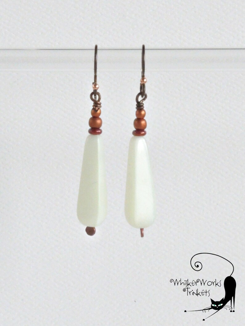 May include: A pair of white teardrop-shaped earrings with copper beads and wire accents.
