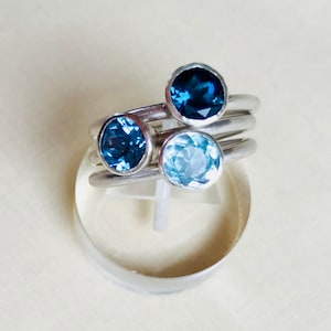 May include: Three silver rings with blue gemstones. The rings are stacked on top of each other. The top ring has a dark blue gemstone, the middle ring has a light blue gemstone, and the bottom ring has a dark blue gemstone.
