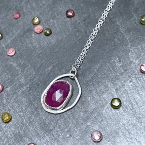 Könnte beinhalten: Eine silberne Kettenkette mit einem Anhänger, der einen tiefvioletten Edelstein in einem silbernen Ovalrahmen trägt.