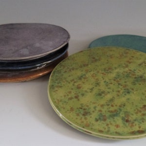 May include: A set of four ceramic plates in various colours, including a stack of three plates in shades of grey, blue, and brown, and a single green plate with brown speckles.