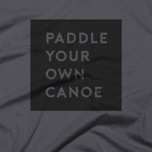 May include: A dark grey t-shirt with the text "Paddle Your Own Canoe" printed in white on a black rectangle.