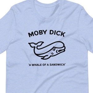 Puede incluir: Camiseta azul claro con un gráfico negro de una ballena y el texto "Moby Dick" y "A whale of a sandwich".