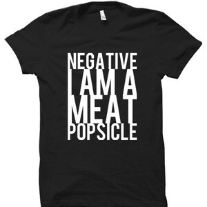 Peut inclure: T-shirt noir avec du texte blanc qui dit "NEGATIVE I AM A MEAT POPSICLE".