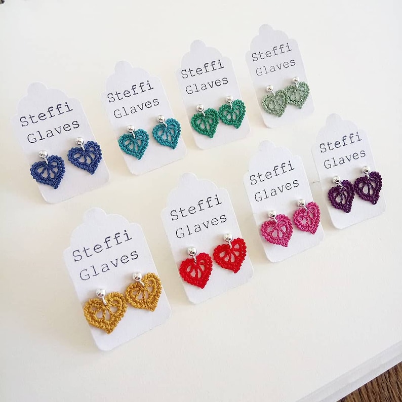May include: Assortment of crocheted heart-shaped earrings in various colors, including red, pink, purple, green, blue, and yellow. Each pair of earrings is displayed on a white card with the text "Steffi Glaves" printed on it.