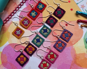 Pode incluir: Um conjunto de 10 pares de brincos de crochê em várias cores, incluindo roxo, verde, vermelho, laranja e amarelo. Cada brinco tem formato quadrado com um design floral no centro.