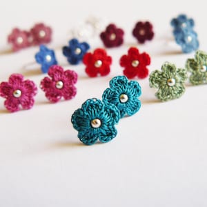May include: Assortment of crocheted flower earrings in various colours, including teal, pink, red, green, and blue. Each earring features a small silver bead in the centre.