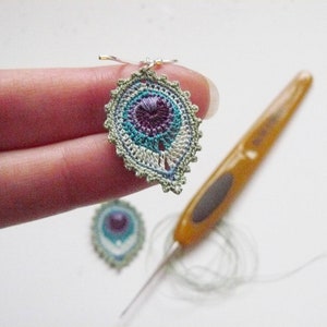 May include: A pair of crocheted earrings with a peacock feather design. The earrings are green, blue, purple, and white. They are hanging from silver hooks.