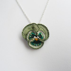 May include: A green crocheted pendant necklace featuring a pansy flower with white, green, and yellow accents.