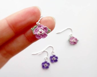 May include: A pair of crocheted flower earrings with silver hooks. One pair is pink with a green leaf and the other pair is purple.