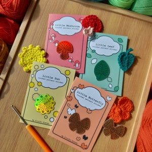 May include: Four colourful crochet pattern stickers featuring a mushroom, leaf, sun, and butterfly. Each sticker has a holographic finish and is labelled with the name of the pattern and the phrase "crochet pattern sticker".