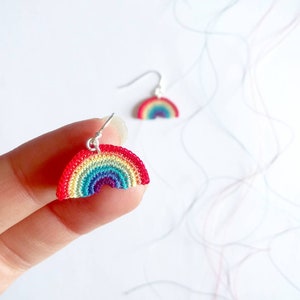 May include: Rainbow crochet earrings with silver hooks. The earrings are small and feature a rainbow design with red, orange, yellow, green, blue, indigo, and violet colors.