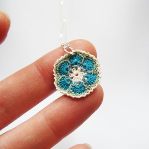 May include: A crocheted flower pendant necklace with a white center and blue and green outer layers.