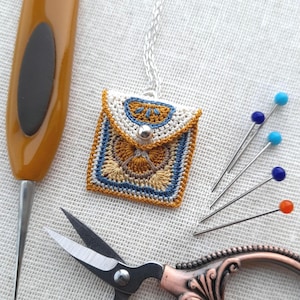 May include: A crocheted pouch necklace with a geometric pattern in shades of blue, brown, and yellow. The pouch is attached to a silver chain.