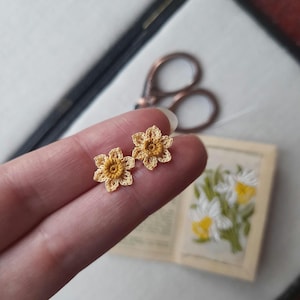 May include: A pair of crocheted daffodil earrings in yellow and cream. The earrings are small and delicate, and they would make a lovely gift for a flower lover.