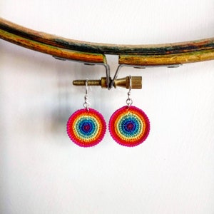 May include: Rainbow crocheted earrings with a beaded center. The earrings are round and have a silver hook.