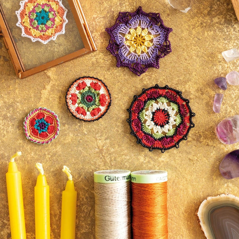 K&ouml;nnte beinhalten: Eine Sammlung von sechs bunten geh&auml;kelten Mandala-Designs mit einer Vielzahl von Farben, darunter Rot, Orange, Gelb, Gr&uuml;n, Blau und Lila. Die Mandalas sind auf einer braunen Oberfl&auml;che mit Garnrollen und anderen Dekorationsartikeln angeordnet.