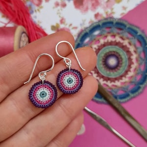 May include: A pair of silver dangle earrings with crocheted purple, pink and green circular charms.