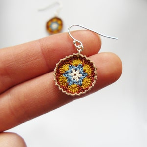 May include: Crocheted flower earrings with a brown, yellow, blue, and white pattern. The earrings are attached to silver hooks.