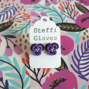 May include: A pair of purple crocheted pansy flower earrings on a white card with the text "Steffi Glaves".