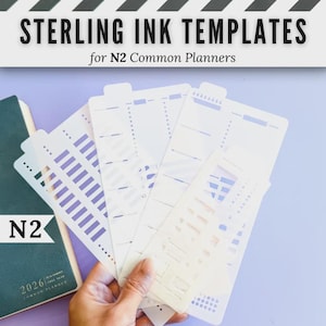 Pode incluir: Um conjunto de estênceis de plástico translúcido rotulados como Sterling Ink Templates for N2 Common Planners, com vários recortes para grades, listas e caixas de seleção, exibidos ao lado de um caderno N2 Common Planner verde escuro 2026.