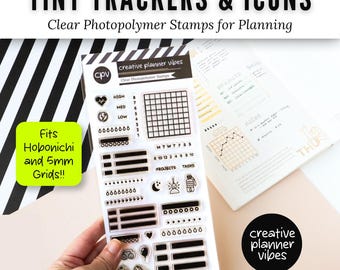 May include: A clear photopolymer stamp set labeled Tiny Trackers & Icons by Creative Planner Vibes. The sheet includes various grid trackers, checklists, water drop icons, and small symbols like a heart, moon, and camera for planner organization.