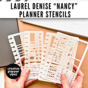 May include: White planner stencils with various shapes and icons, including houses, arrows, and banners. The stencils are held in a person's hands, with a black circle that says "creative planner vibes" in the lower left corner. The text "LAUREL DENISE "NANCY" PLANNER STENCILS" is at the top.