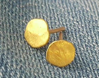 May include: A pair of gold-toned stud earrings with a hammered finish. The earrings are small and round, and they are set on a silver post.