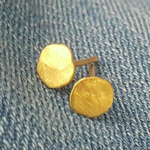Peut inclure: Une paire de boucles d'oreilles clous dorées avec une finition martelée. Les boucles d'oreilles sont petites et rondes, et elles sont montées sur une tige en argent.