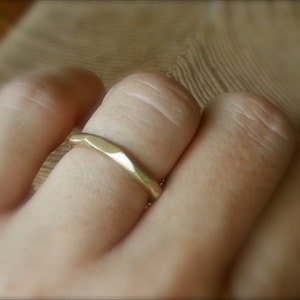 May include: A gold band ring with a hammered texture. The ring is worn on a finger.