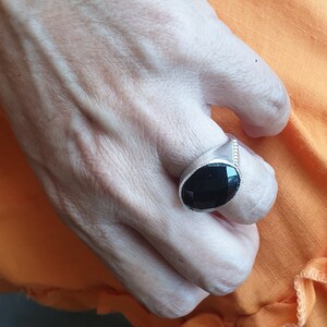 May include: A silver ring with a black oval gemstone. The ring is on a person's finger.