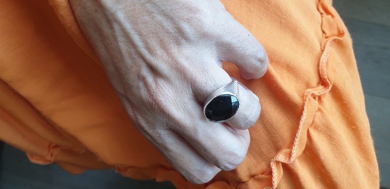 May include: A silver ring with a black oval gemstone. The ring is on a person's finger.