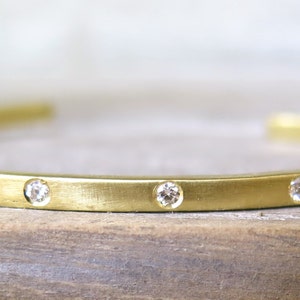 May include: A gold bangle bracelet with a brushed finish and small diamonds set along the top edge.