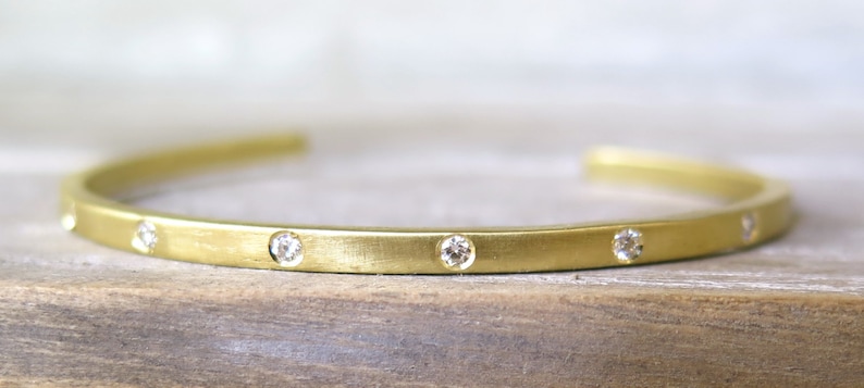 May include: A gold bangle bracelet with a brushed finish and small diamonds set along the top edge.