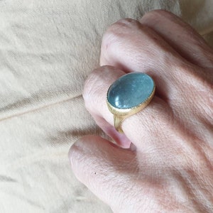 May include: A gold ring with a large oval aquamarine gemstone. The ring is set in a simple band with a textured edge.