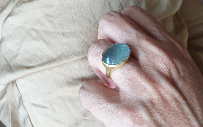 May include: A gold ring with a large oval aquamarine gemstone. The ring is set in a simple band with a textured edge.