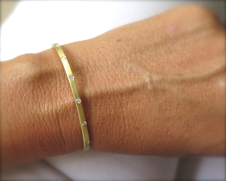 May include: A gold bangle bracelet with small diamonds set into the band.