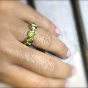 May include: A gold ring with a row of green gemstones. The ring is on a person's finger.