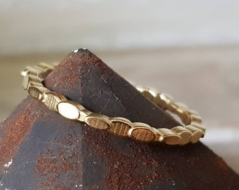 Può includere: Un anello d'oro con un design unico caratterizzato da una serie di maglie ovali. L'anello è mostrato su una superficie marrone testurizzata.