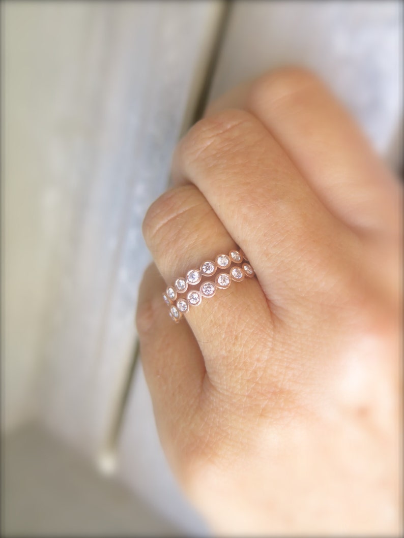May include: A rose gold ring with two rows of bezel-set round diamonds.